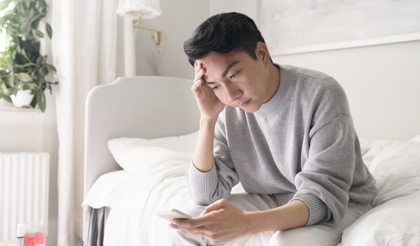 Ung man med mobiltelefon sitter på en säng.