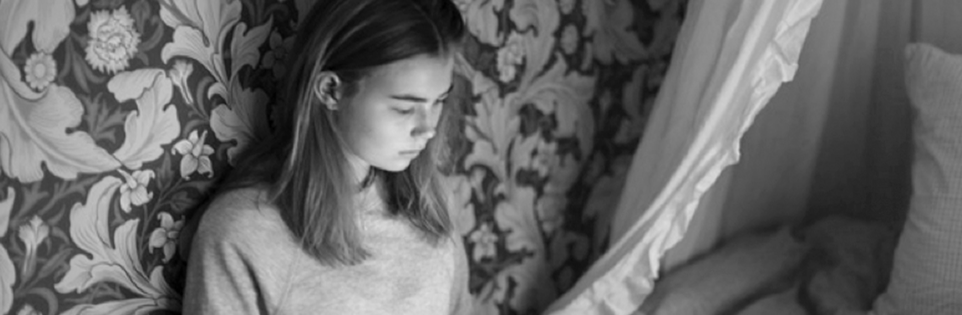 Flicka sitter i sängen och kollar på sin dator.