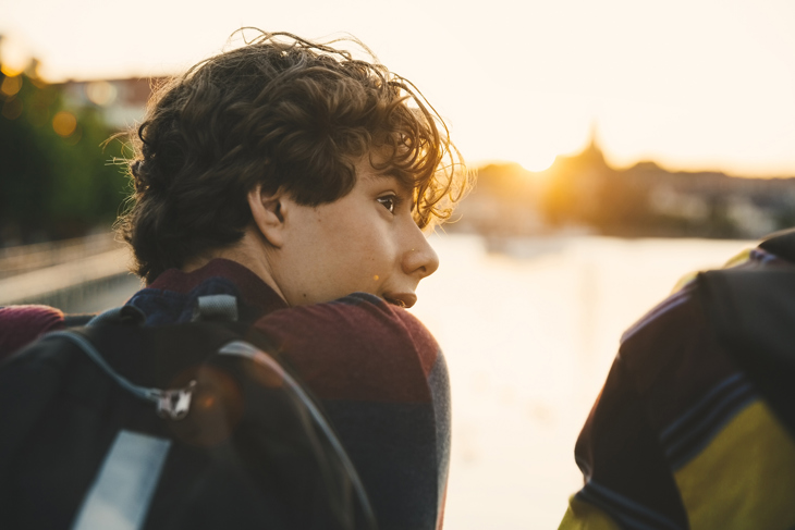 Ung kille sitter framför vatten med sin vän.