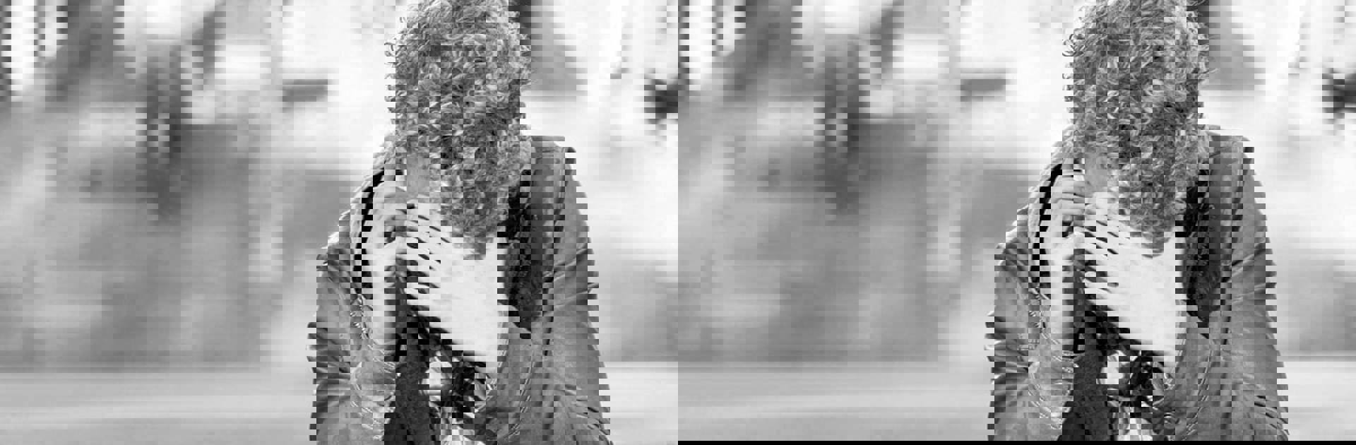 En ung man som sitter och pratar i mobiltelefon med en hand framför ansiktet.