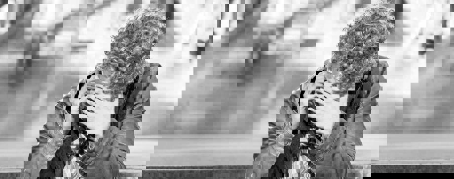 Svartvit bild på en ung man sitter och pratar i mobiltelefon med en hand framför ansiktet.