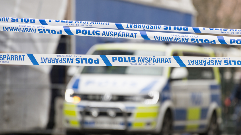 Band som visar att ett område är avspärrat område och en polisbuss i bakgrunden.